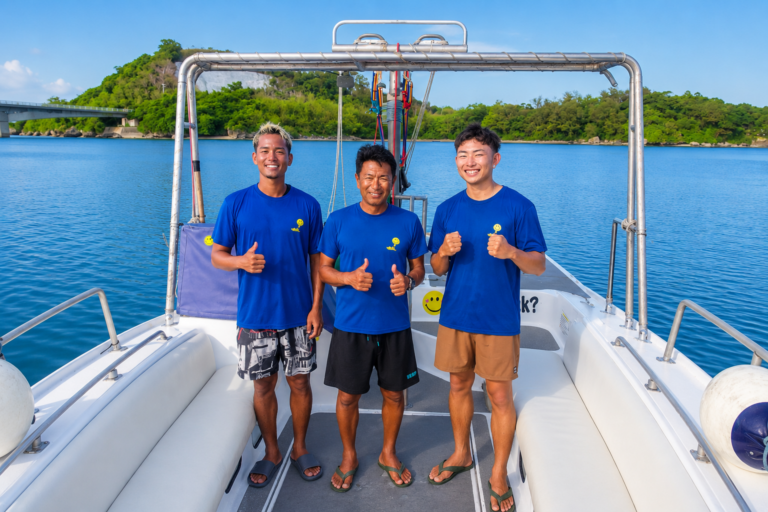 沖縄の海でボートから笑顔で挨拶するマリンアイランドスタッフ3名